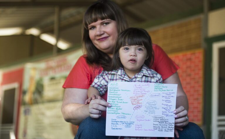 A young girl with Down syndrome and other special health care needs and her mother hold up a copy of her care map.