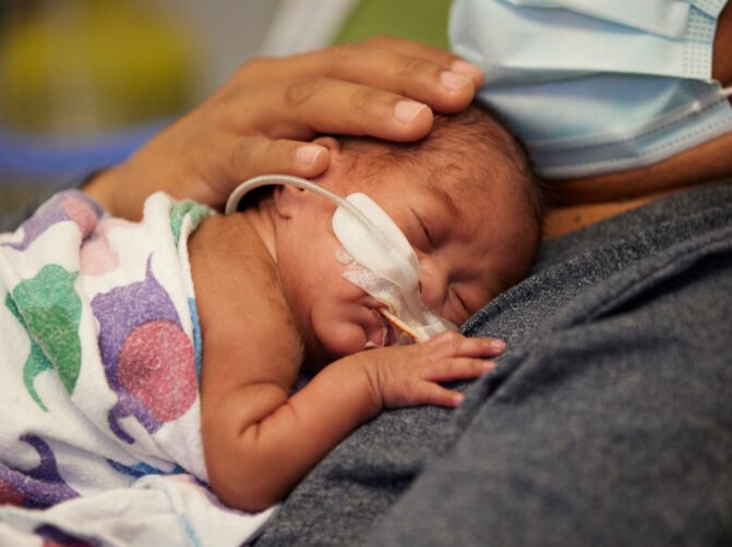 A newborn NICU baby lays on his fathers chest