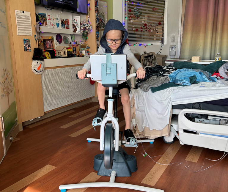 A young patient riding his stationary bike in his hospital room.