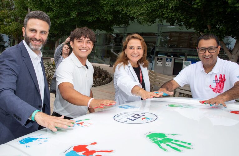 Hyundai Hope on Wheels representatives, patient Tyler, and Dr. Raya Saab stand in front of a Hyundai vehicle and place colorful handprints on the hood.