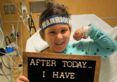 Cancer patient flexing their arm, holding a motivational sign, and smiling at the camera.
