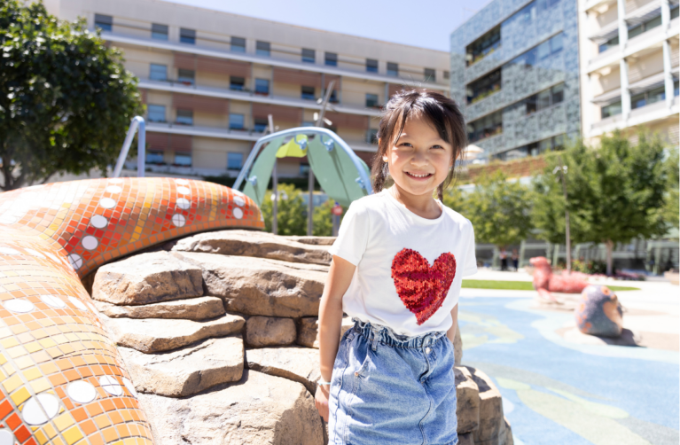 Pediatric patient stands smiling at the camera in the Dawes Garden at Stanford Children’s Hospital.
