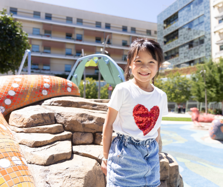 Pediatric patient stands smiling at the camera in the Dawes Garden at Stanford Children’s Hospital.