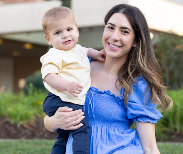 Former Packard Children's patients, parent and child, sitting in front of Packard Children's and smiling at the camera.