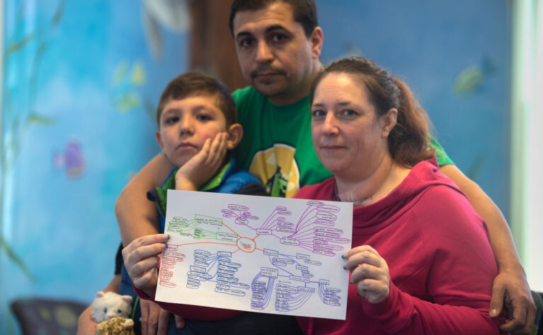A boy with special health care needs sits on his father's lap, while his mother, seated next to him, holds up his care map.