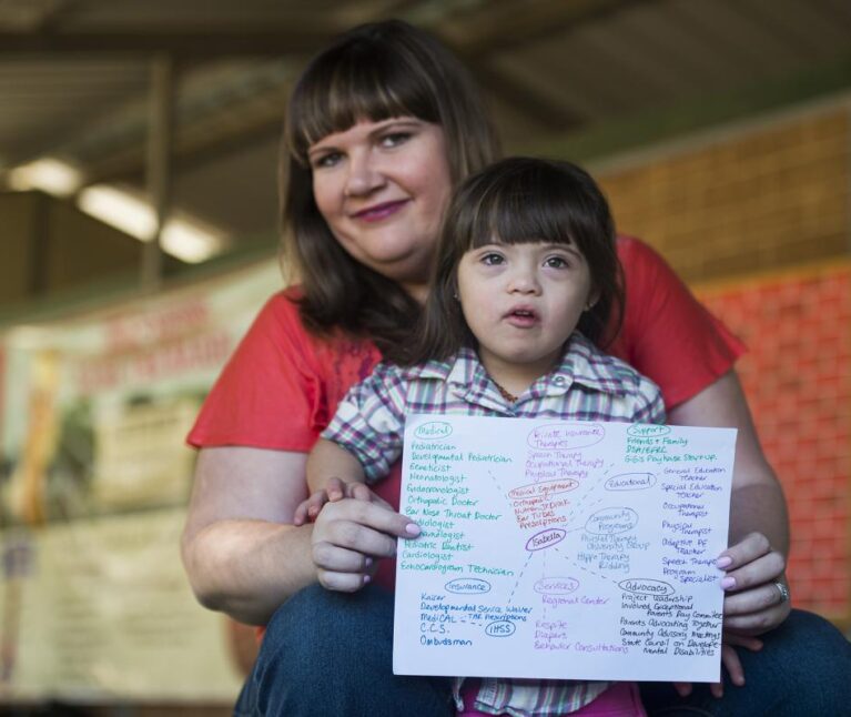 A young girl with Down syndrome and other special health care needs and her mother hold up a copy of her care map.