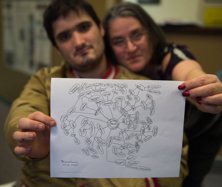 A mom and her adult son with special health care needs hold up a copy of his care map.