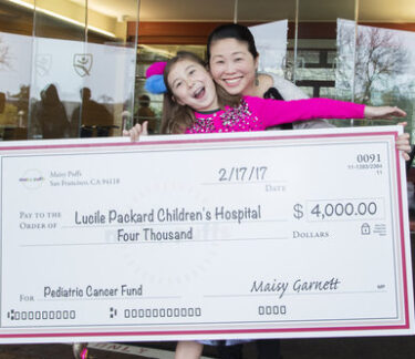 A young girl and her mother hold an oversized check showing the money she raised for the children's hospital