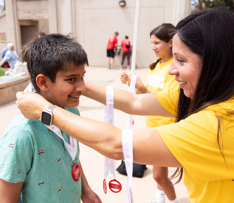 A volunteer hangs a medal on a young person at Summer Scamper