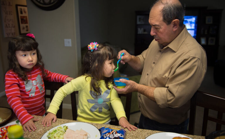 Grandfather helping to feed his twin CYSHCN granddaughters