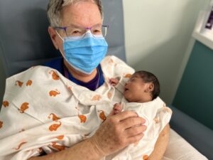 Older woman wearing a mask holding baby in the NICU.