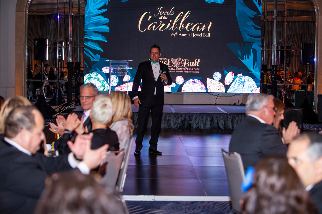 An event emcee holds a microphone on stage at the 67th annual Jewel Ball