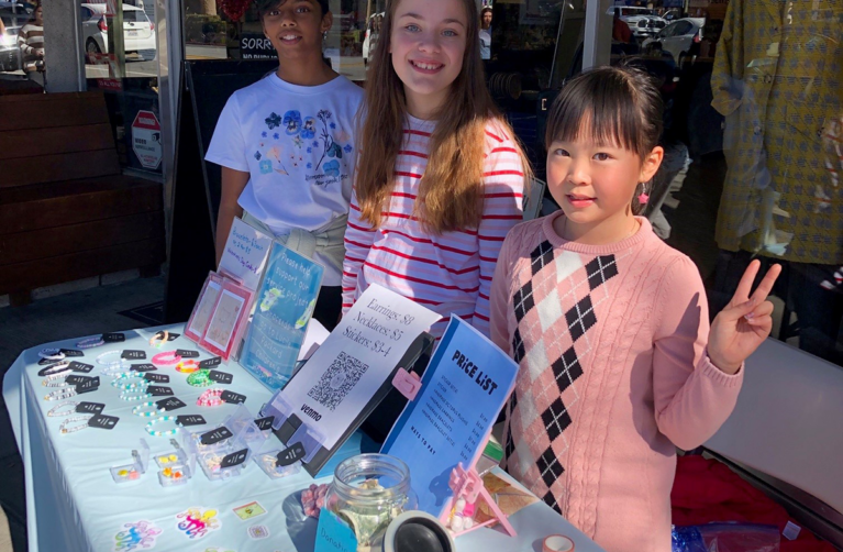 Three girls pose by their table where they are selling crafts to raise money for the children's hospital.