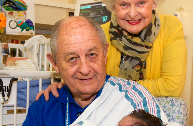 Married couple Pat Rice and Claire Fitzgerald holding a newborn baby in a hospital room at Stanford Children's Hospital.