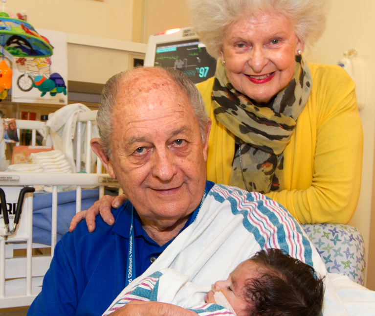 Married couple Pat Rice and Claire Fitzgerald holding a newborn baby in a hospital room at Stanford Children's Hospital.