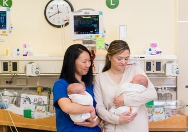A nurse and a mother hold two babies in a hospital room in the NICU.