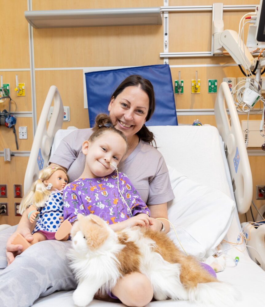 Ryan, age, 6, seated on a hospital bed with her mom.