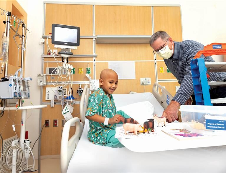 Photo of a patient in his hospital bed wearing scrubs and a chaplain playing with him.