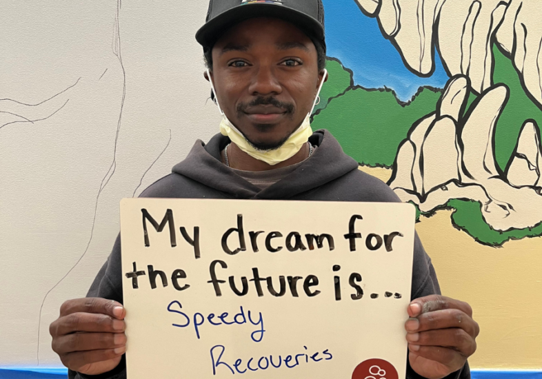 Hospital staff holding a white board that reads "My dream for the future is speedy recoveries."