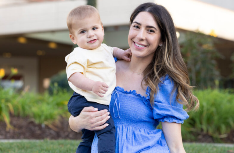 Former Packard Children's patients, parent and child, sitting in front of Packard Children's and smiling at the camera.