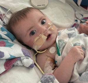 Infant heart patient in a hospital bed during treatment, covered with blankets.