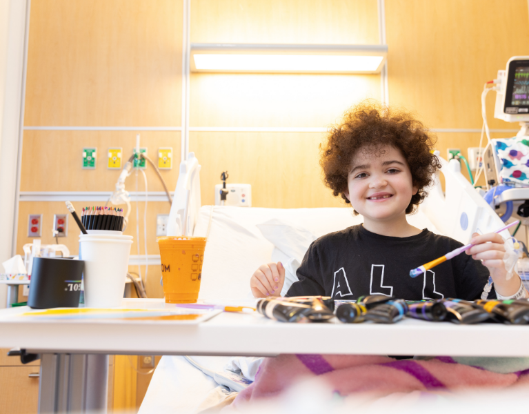 Pediatric patient engaged in art therapy, painting in a hospital bed and smiling in a bright, warm hospital room..