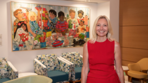 Dr. Tanja Gruber poses in the BASS Center lobby at Lucile Packard Children's Hospital Stanford. Dr. Gruber wears a sleeveless red dress and smiles brightly at the camera.
