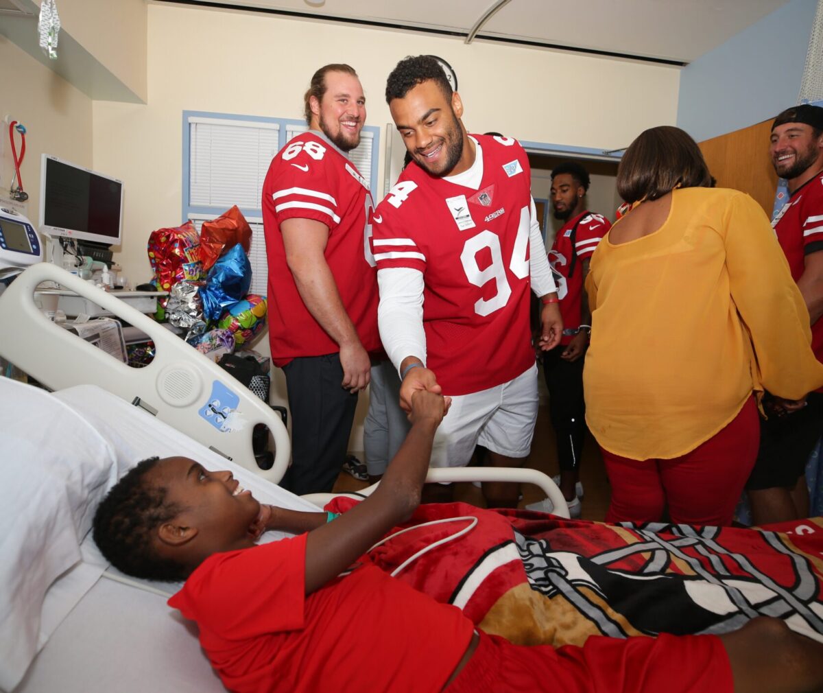 Football player and child shake hands in hospital room.