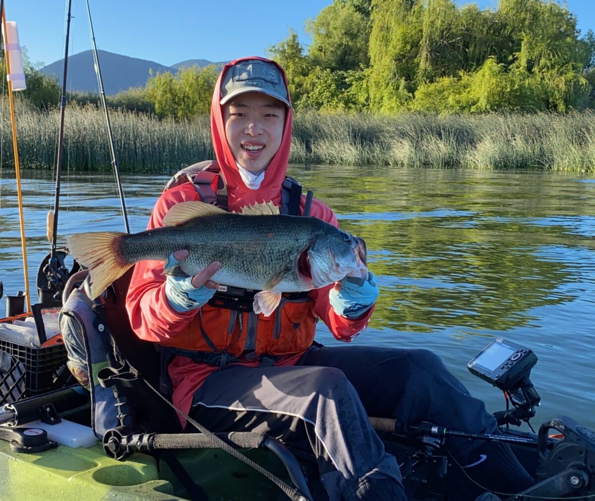 Dean Wu holding a fish sitting on a fishing boat.