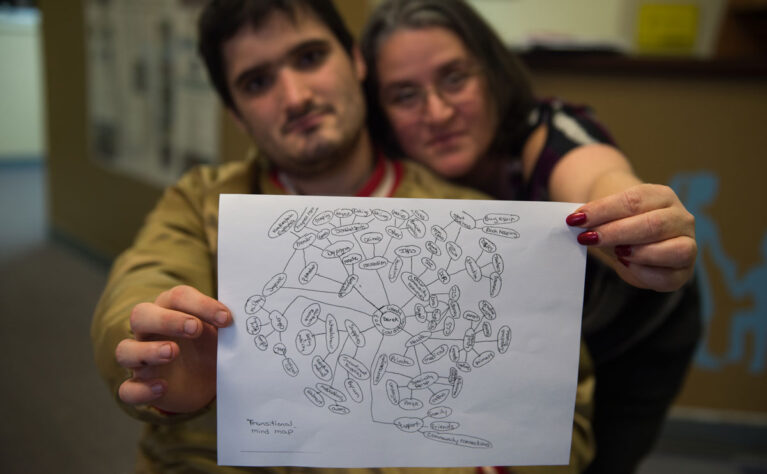 A mom and her adult son with special health care needs hold up a copy of his care map.