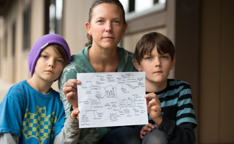 Young brothers with special health care needs stand on either side of their mother while she holds a copy of their care map.