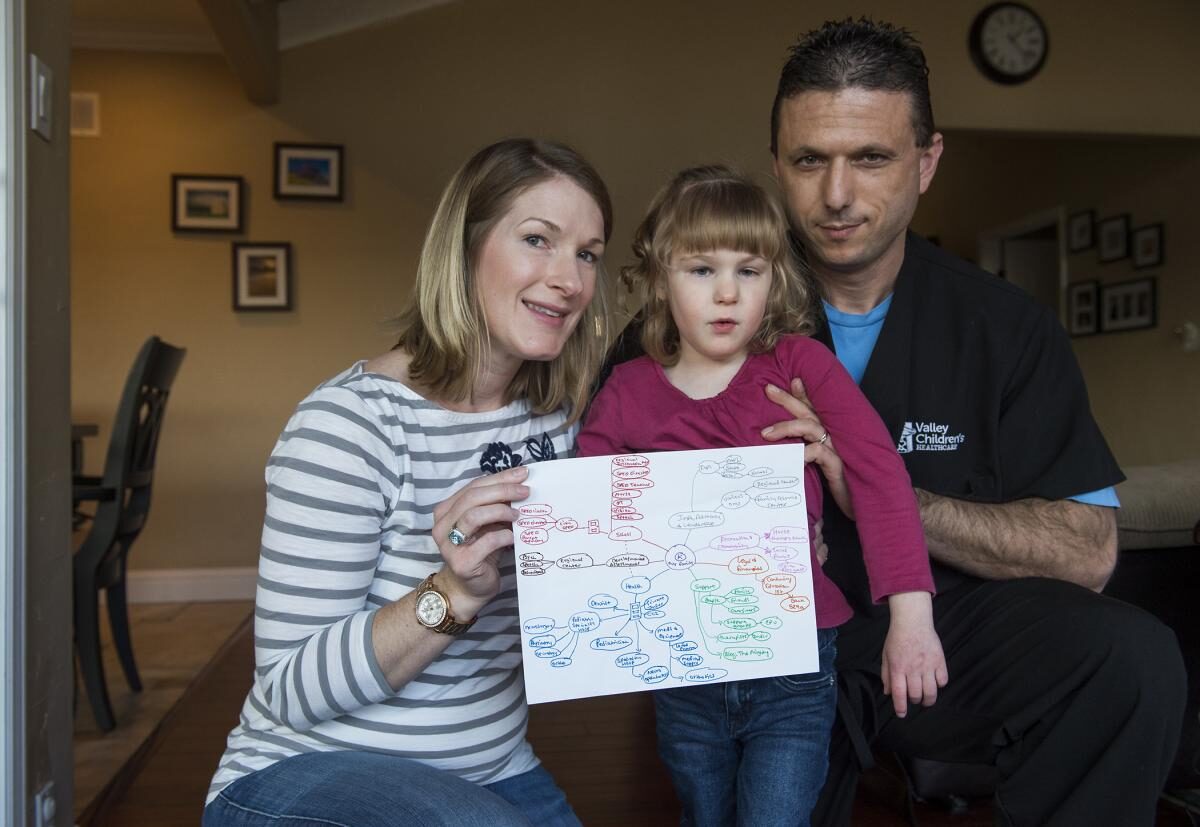 A young girl with special health care needs and her mother hold up a copy of her care map. There is an adult man also standing with them.
