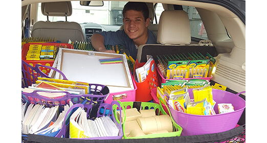 Pediatric patient smiling at camera sitting in car full of school supplies.