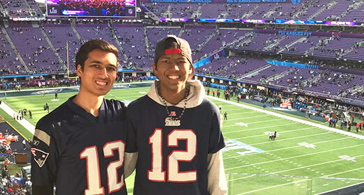 Two friends standing together in a football stadium smiling at the camera.