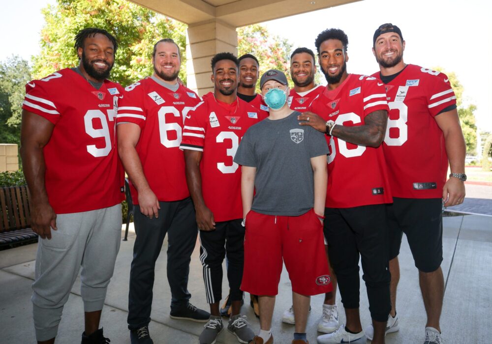 Group of football players and young boy pose for camera.