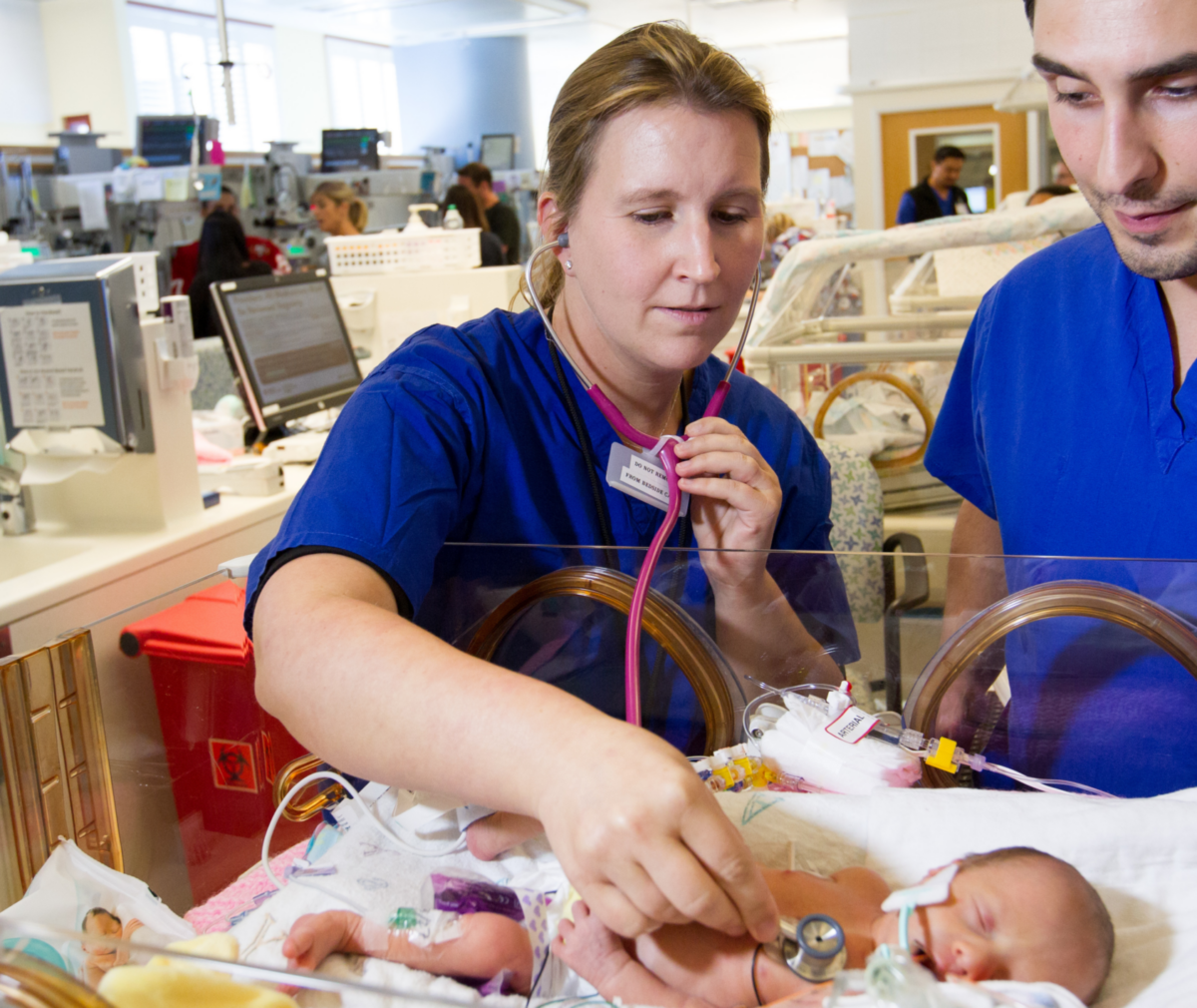 Nurses with stethoscope checking baby's heartrate in NICU.