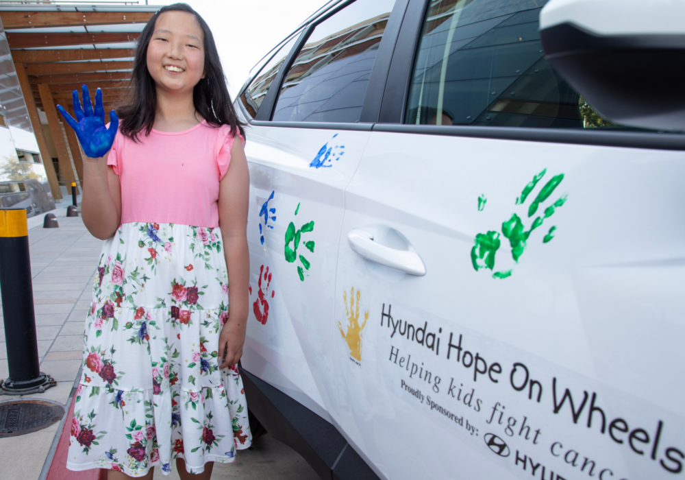 Zoe participating in Hyundai Hope On Wheels with blue painted hand standing next to a car.