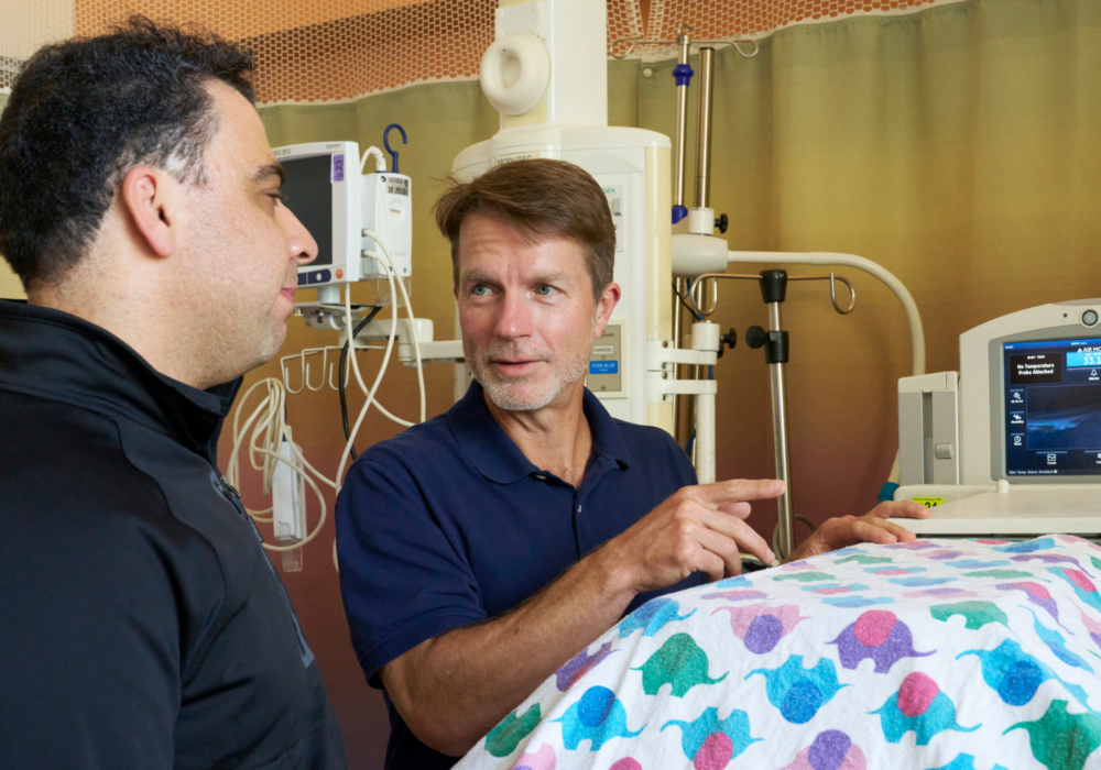 Nima and associate in NICU room, talking over hospital bed.