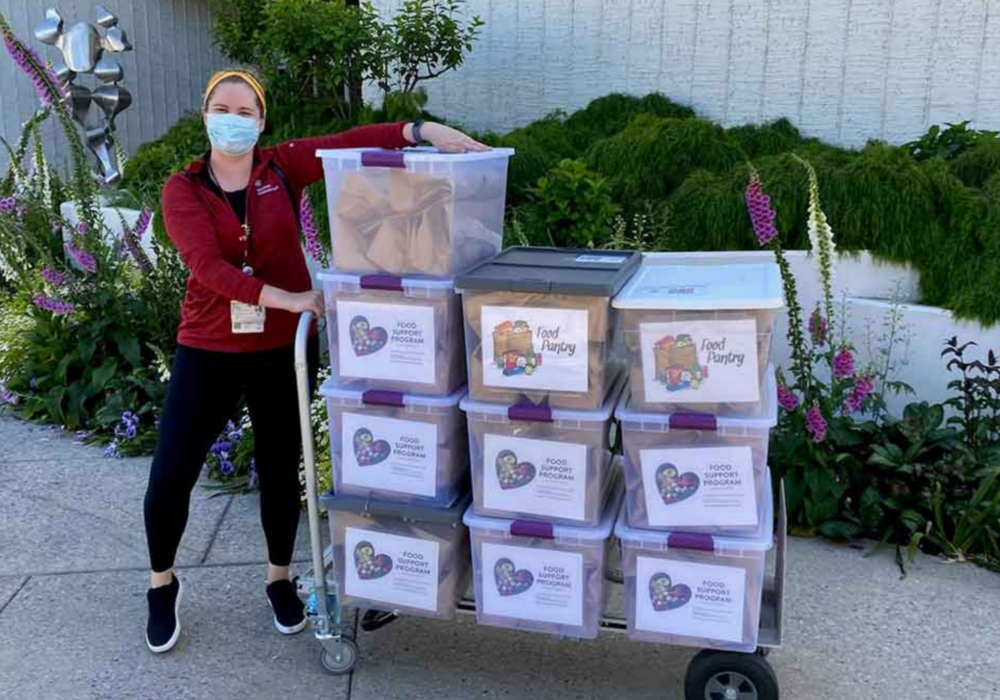 Volunteer standing with dolly of food donations.