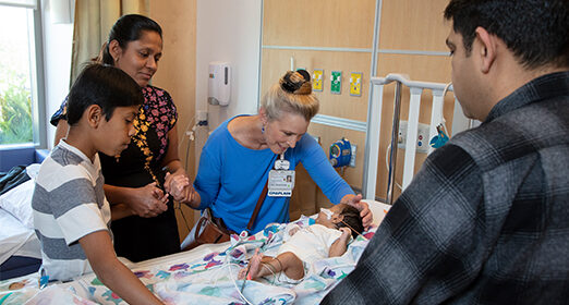Adults surrounding an infant patient in a hospital room.