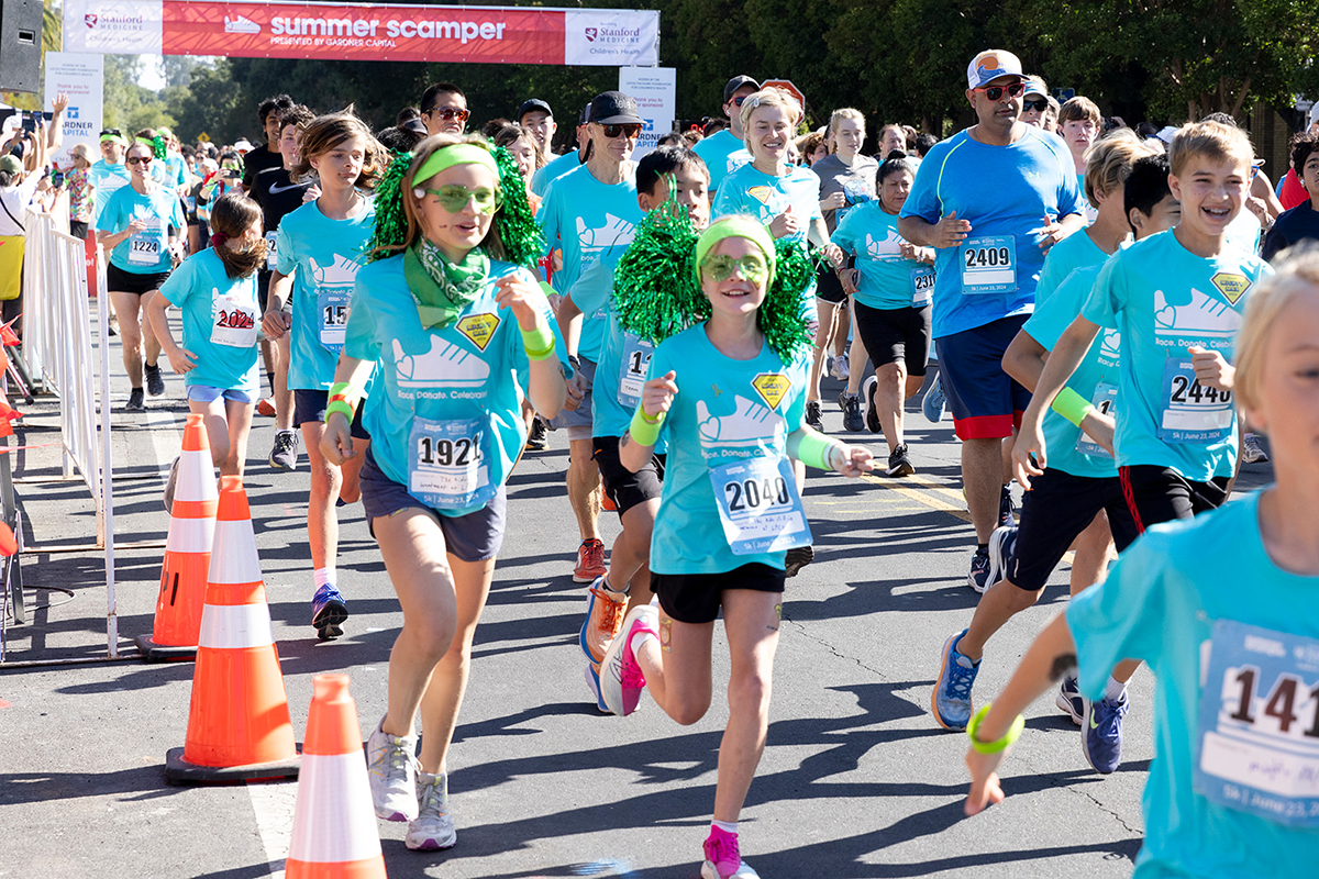 Two girls smiling at the camera among other participants as they run in Summer Scamper at Stanford University.