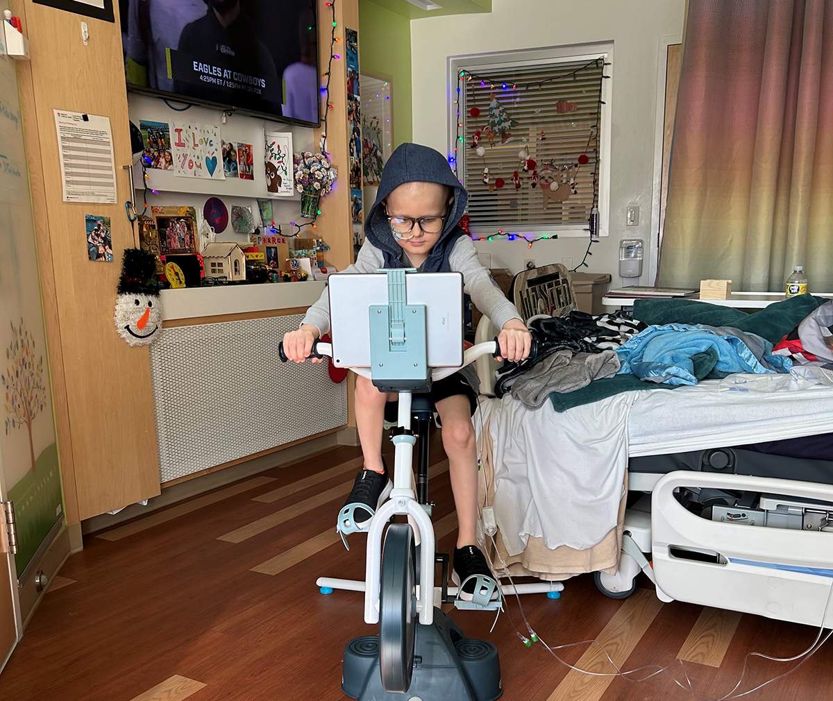 A young patient riding his stationary bike in his hospital room.