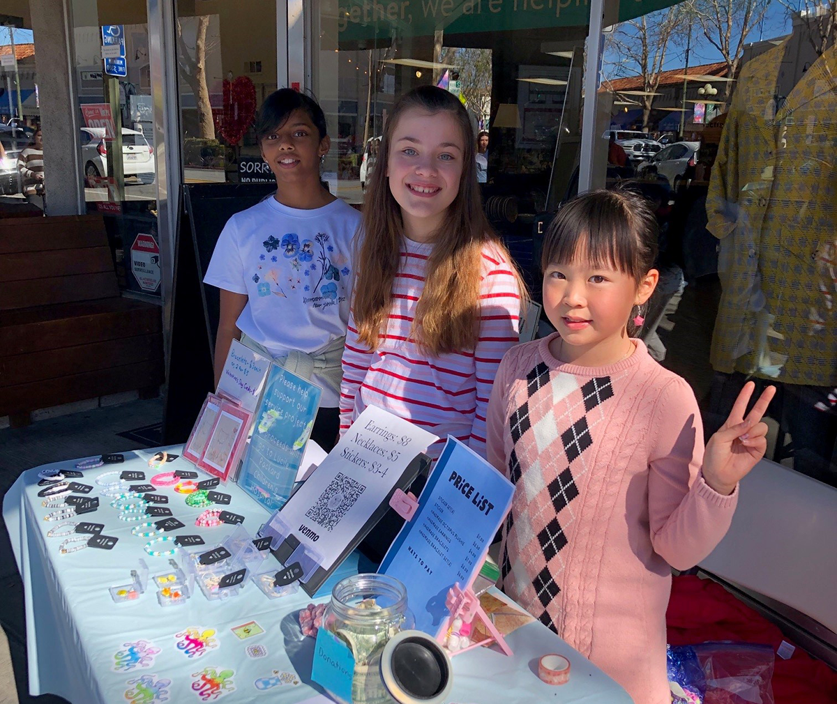 Three girls pose by their table where they are selling crafts to raise money for the children's hospital.