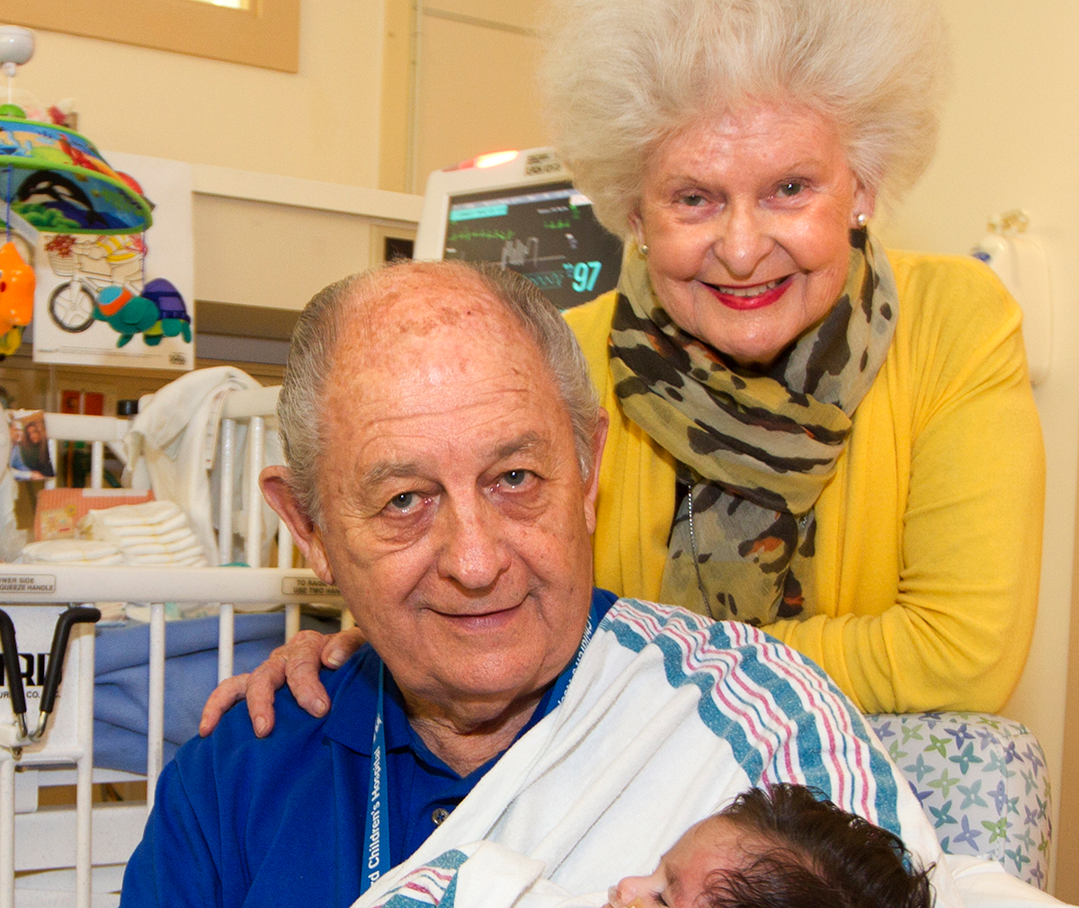 Married couple Pat Rice and Claire Fitzgerald holding a newborn baby in a hospital room at Stanford Children's Hospital.
