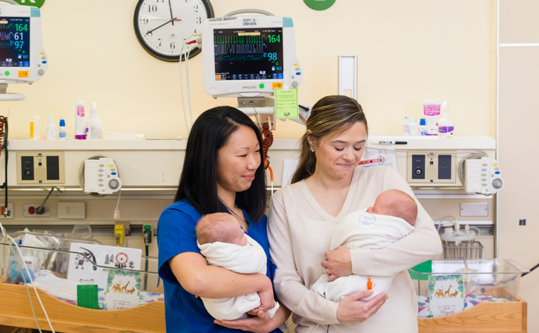 A nurse and a mother hold two babies in a hospital room in the NICU.