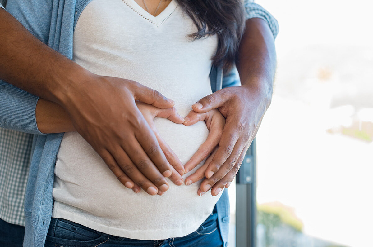 Pregnant woman and partners hands resting on stomach of her belly.