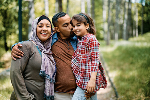 Happy Middle Eastern parents with daughter enjoying in family day in nature. Father is holding and kissing his daughter while mother is looking at camera.