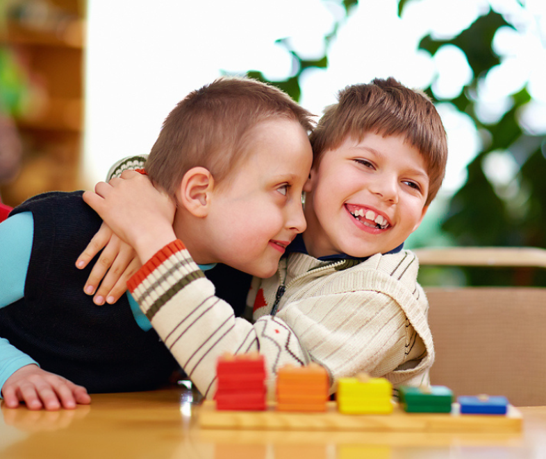 Two young boys smiling and hugging while playing with colored blocks.