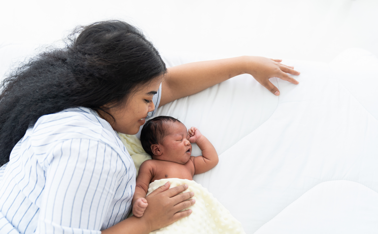 A mother cuddles up with her newborn baby on a bed.