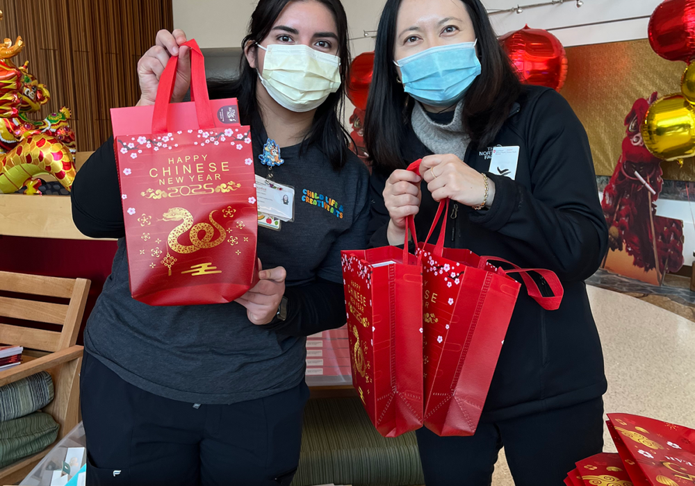 Two women hold up red gift backs at a hospital event.